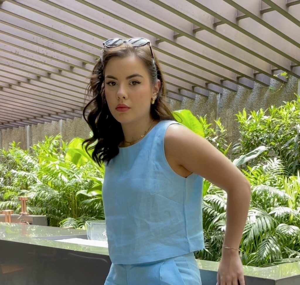 Sophia Ferreira posa com um conjunto azul sofisticado, destacando um look de moda fashionista em um ambiente elegante e verde.
