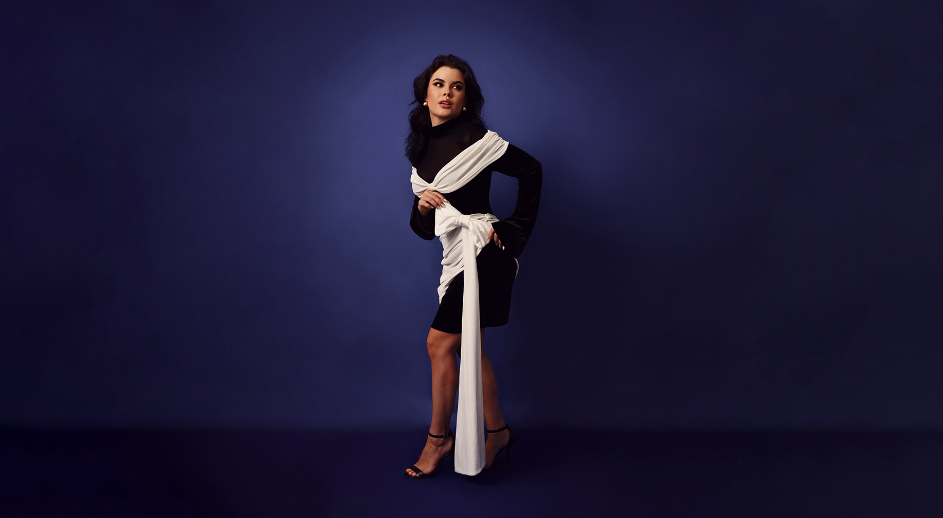 Sophia Ferreira em um vestido sofisticado preto e branco, posando com elegância e confiança contra um fundo azul, representando o luxo, branding de influência e sofisticação no mercado premium.