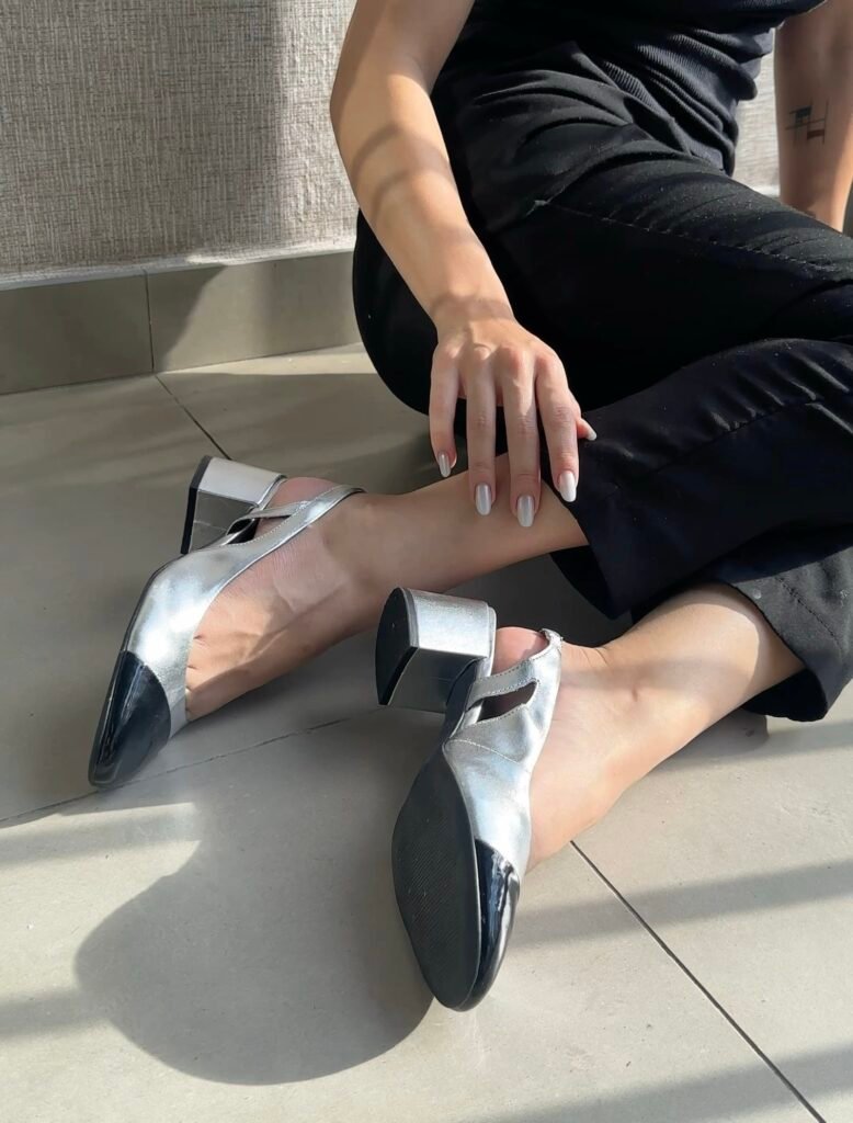 Modelo de sandália slingback Giulia Domna em prata e preto, realçando elegância e versatilidade.