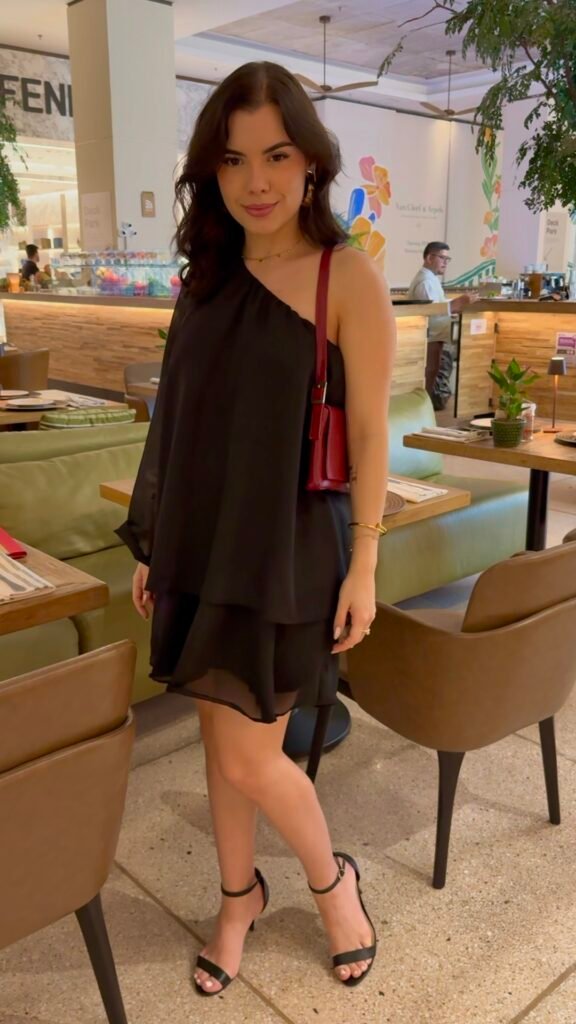 Sophia Ferreira em um restaurante vestindo um elegante vestido preto de um ombro só da New Bossa.