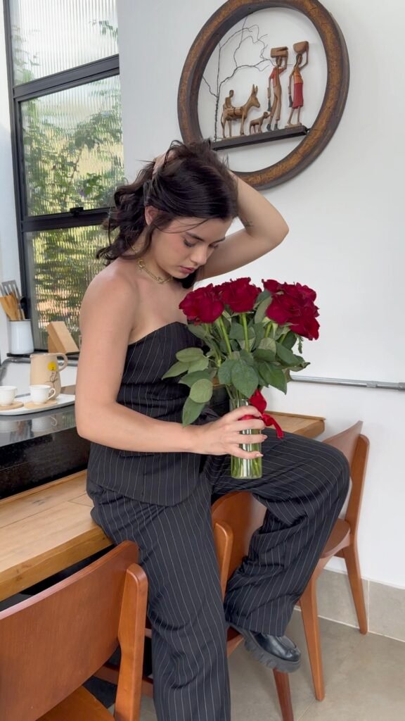 Sophia Ferreira posa sentada em um sofá elegante, usando um vestido vermelho de manga única da New Bossa.