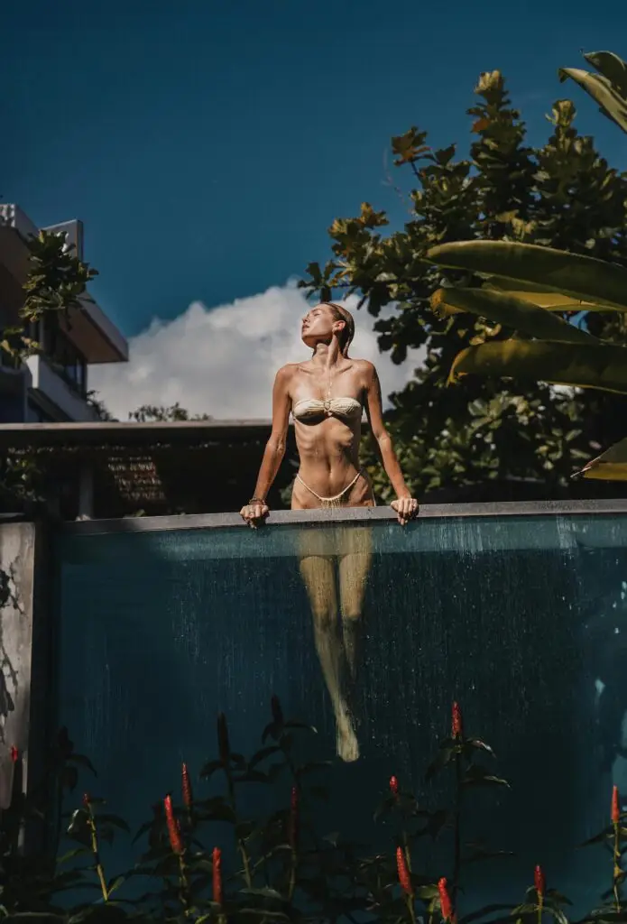 Mulher em biquíni dourado emergindo de uma piscina de borda infinita, refletindo o conceito de luxo, bem-estar e exclusividade.