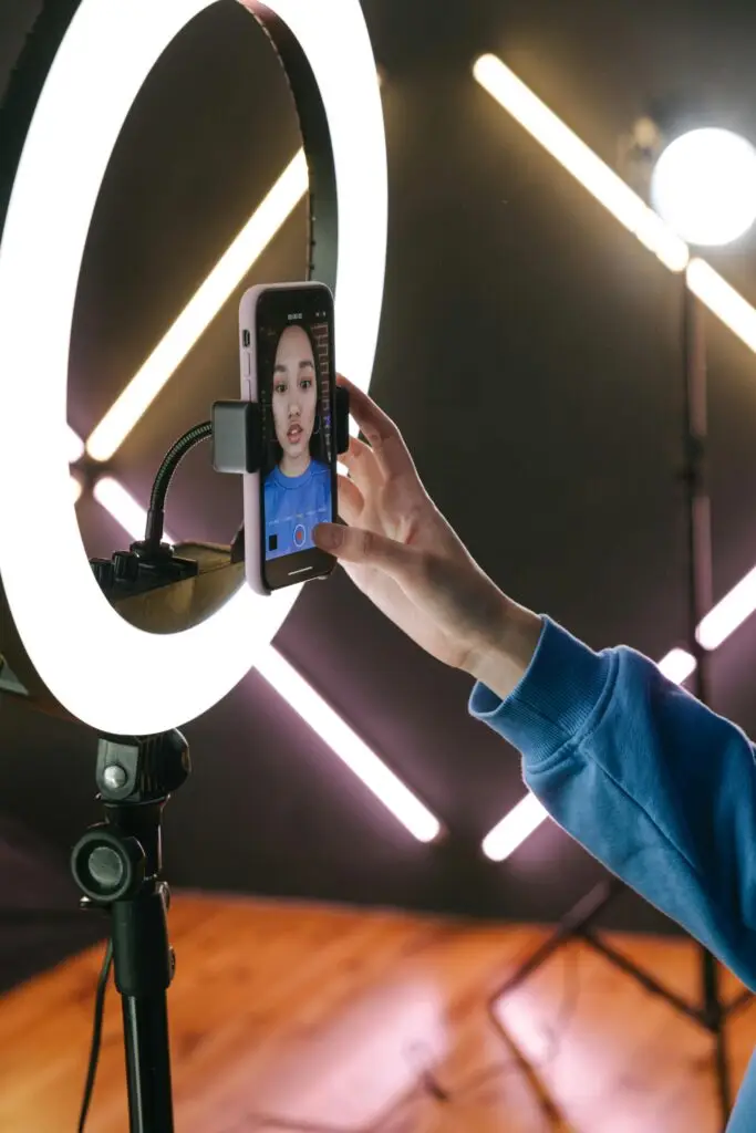 Criadora de conteúdo gravando um vídeo com smartphone e ring light em um estúdio moderno, destacando a importância da iluminação na produção de conteúdos digitais.