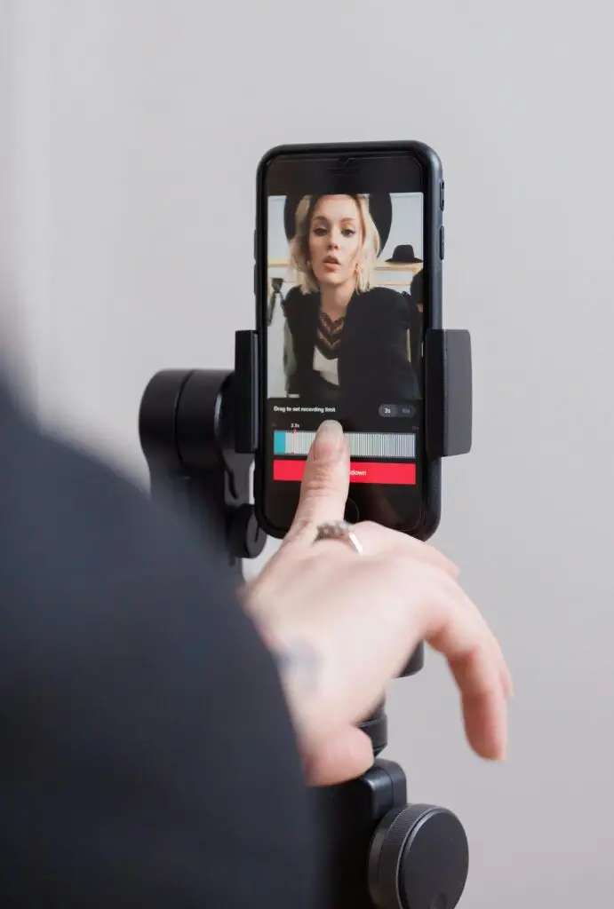 Criadora de conteúdo gravando um vídeo no smartphone, utilizando um tripé para estabilidade e um fundo minimalista, otimizando a produção de conteúdos para redes sociais.